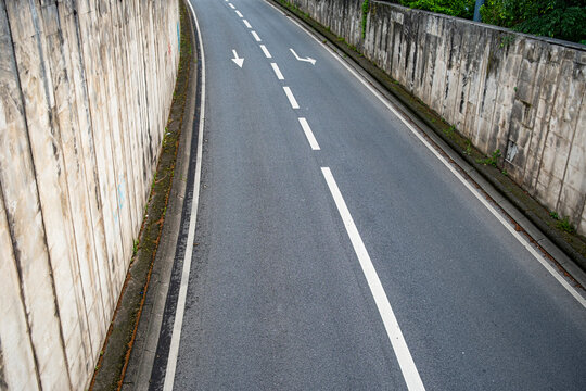 Empty curving urban road with white lane markings between concrete walls creating strong perspective and a clean modern transport scene