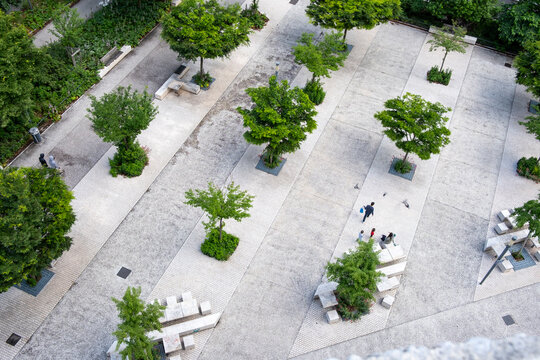 Elevated view of a landscaped urban plaza with trees benches and pedestrians showing green public space integrated into a modern city environment