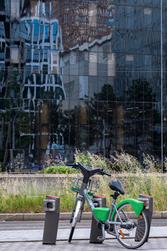 Public rental bicycles parked beside a reflective building facade showing shared urban mobility in a contemporary city environment with modern architecture