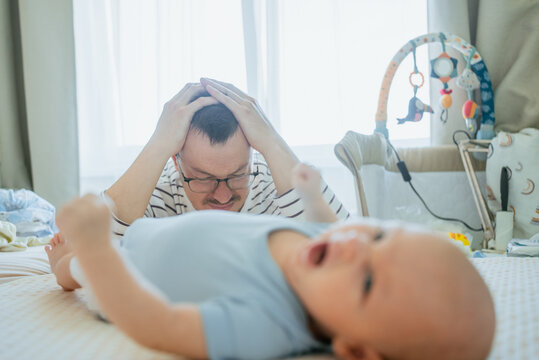 Young father feeling overwhelmed and highly stressed by the relentless crying of his baby, suffering from exhaustion, a severe headache, and signs of depression due to the demands of new parenthood