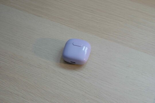 Purple wireless earbuds case on wooden surface in bright lighting