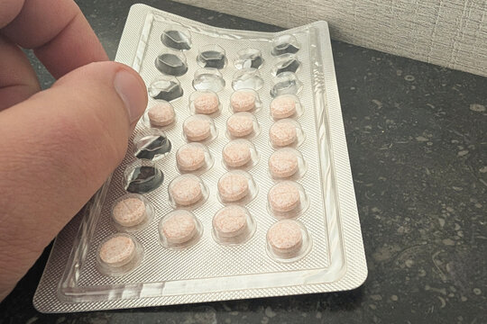 Hand holding a blister pack of tablets on a dark surface