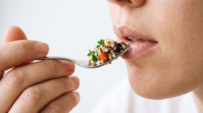 Healthy eating brings joy. A metal fork lifts a balanced, fresh quinoa and herb salad toward an open mouth for a wholesome, nutritious meal.