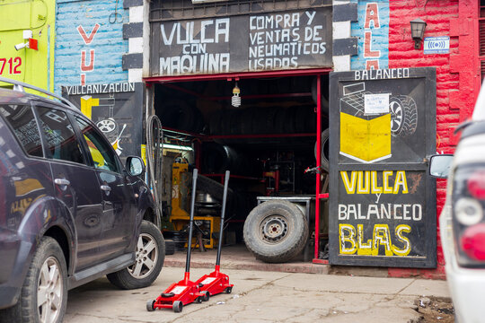 A small tire repair shop in Santiago, Chile displays painted signs, used tires, hydraulic jacks, and a parked car at its entrance