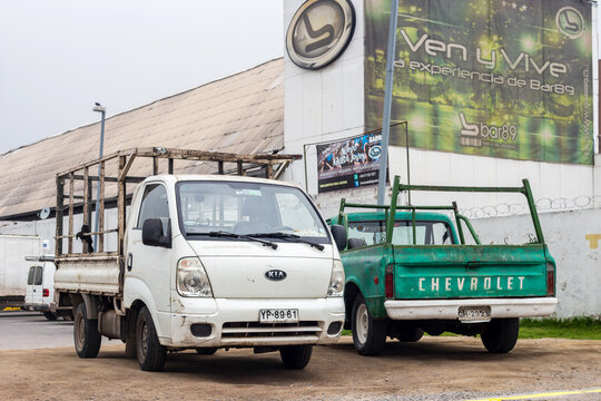 Two work pickup trucks with metal frames are parked outside the Bar89 venue in Santiago, Chile, contrasting everyday labor with nightlife advertising