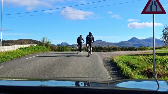 Cyclists ride along a road near Opdol through the beautiful Lofoten landscape with green nature and an impressive mountain backdrop in Northern Norway.