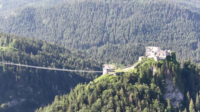 Ehrenberg castle ruins and suspension bridge span forested mountains near Reutte, Austria, aerial drone shot of medieval fortress in Tirol Alps.