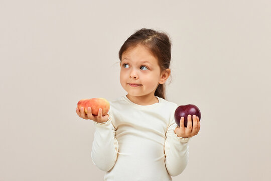 Little girl choosing between peach and red apple