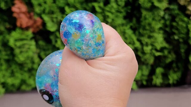 blue glitter kawaii squishy toy with cat ears and cute smiley face in yellow container held in hand, sparkly round ball outdoors