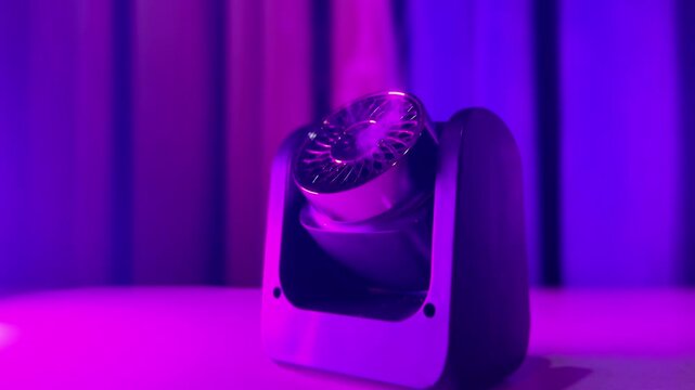 Close-up of a modern black aroma diffuser emitting a thin trail of mist indoors. The sleek electronic device sits on a white surface, illuminated by vibrant purple neon studio lighting.