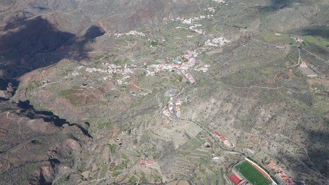Aerial drone push in shot revealing Tejeda, a picturesque mountain village on Gran Canaria. The stunning landscape features terraced fields and houses.