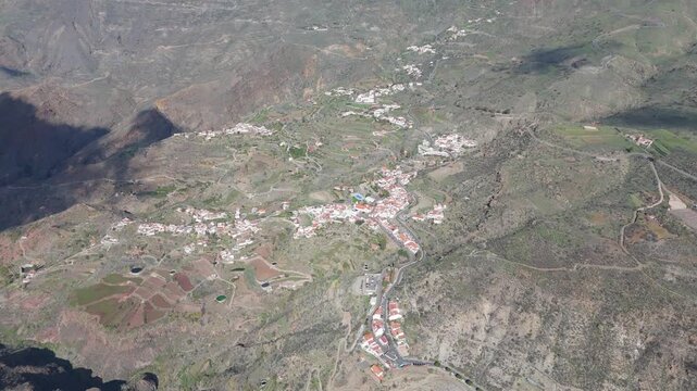 Aerial view of Tejeda village nestled in a rugged mountain valley on Gran Canaria. Pan left reveals houses and terrace farming.