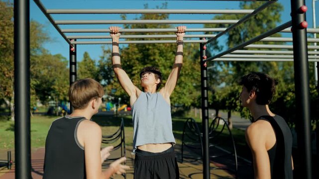 Teen boy team training on monkey bars at the outdoor street fitness ground.