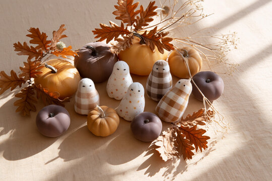 Decorative autumn pumpkin arrangement with plaid and speckled fabric gourds, oak leaves, dried grasses, warm sunlight, and rustic seasonal tabletop still life