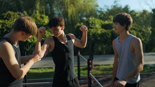 Adolescent boys flexing biceps and checking muscles at the sports park.