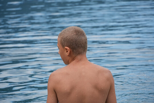 Wet boy seen from behind standing by a lake