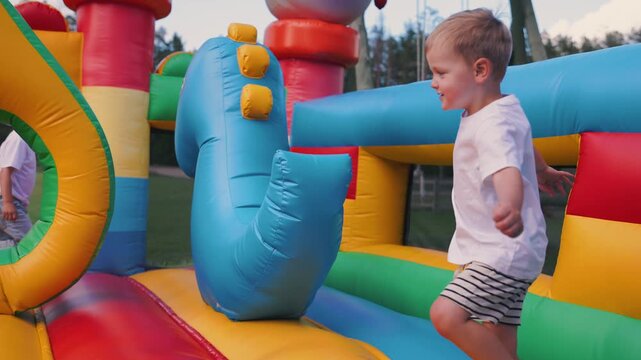 Young boy playing in colorful inflatable bounce house, climbing over bright red cushions and exploring the vibrant structure in a sunny outdoor setting