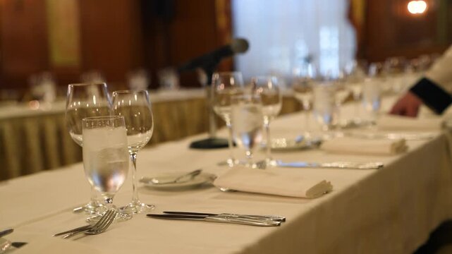 Cinematic footage of an elegant banquet table setting with crystal glassware, silverware, and a microphone, perfect for formal events and weddings.
