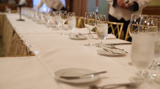 Cinematic footage of an elegant banquet table setting with crystal glassware, silverware, and a microphone, perfect for formal events and weddings.
