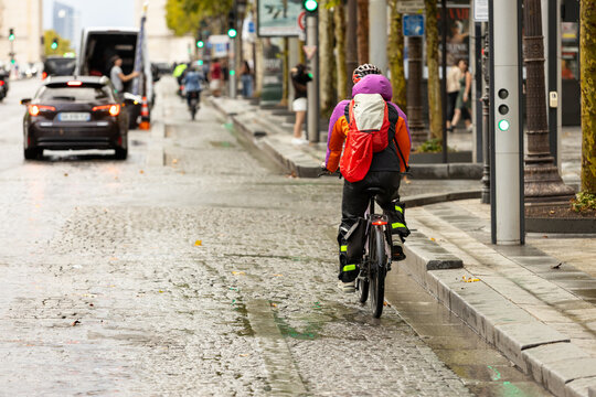 Cyclist riding through rainy Paris on the Champs-&Eacute;lys&eacute;es, sustainable urban transportation, active mobility, and everyday commuting