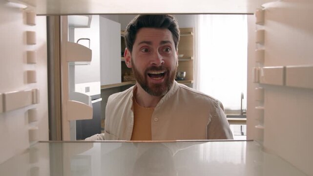 Hungry confused Caucasian man looking into empty fridge hoping food appears in kitchen funny male guy opening again wishing miracle meal no products delivery shopping service POV inside refrigerator