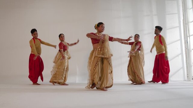 A group of Indian dancers is performing a traditional dance routine in a brightly lit studio