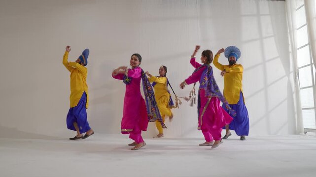 Indian dancers are energetically performing traditional Bhangra dance indoors