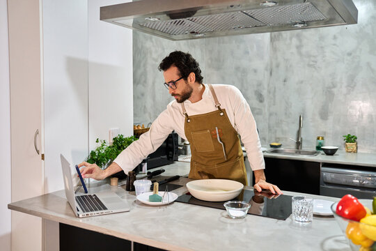 Man learning recipe watching laptop in kitchen