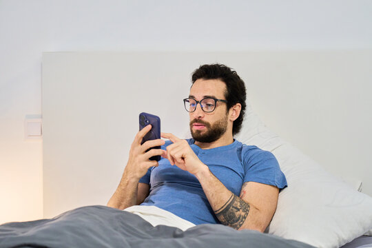 Man relaxing in bed using smartphone in morning
