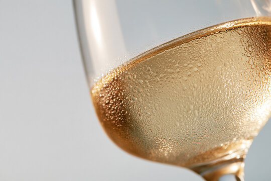 Macro close-up of a chilled white wine glass with fine condensation droplets, pale golden tones, bright clean background, soft even lighting, shallow depth of field, white wine, pr