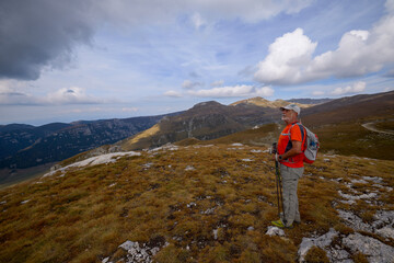 Obraz premium a 75-year-old man hiking in the mountains with poles, a backpack, and mountain gear on a beautiful September day