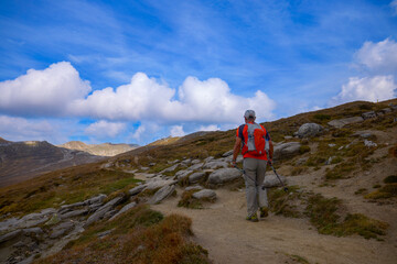 Obraz premium a 75-year-old man hiking in the mountains with poles, a backpack, and mountain gear on a beautiful September day