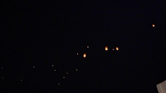 Glowing paper sky lanterns floating upward in night sky during festival celebration, warm amber light inside each lantern, scattered upward composition with serene hopeful atmosphere