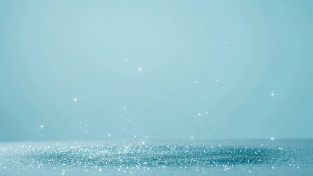 Silver glitter particles floating above a reflective surface, light blue background