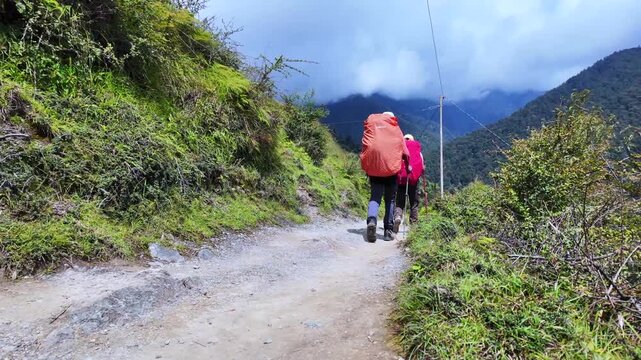 Two Trekkers with Trekking Poles and Rain-Covered Rucksacks Walking Ahead on Mountain Trail