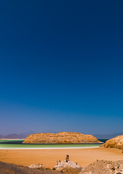 A rocky outcrop rises from turquoise water bordered by white salt deposits, Dikhil Region, Lake Assal, Djibouti