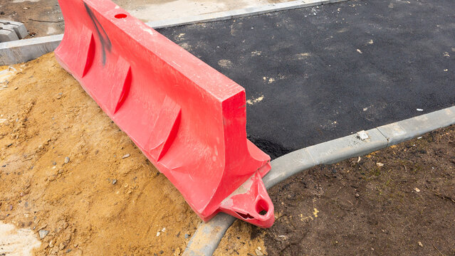 Red temporary safety barrier placed near fresh asphalt during road construction, representing infrastructure maintenance, street repair, traffic safety and urban improvement projects
