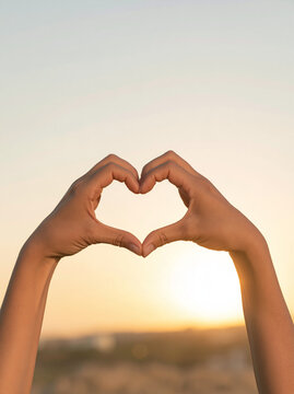 Hands Making Heart Shape Against Sunset Sky as Symbol of Love and Hope