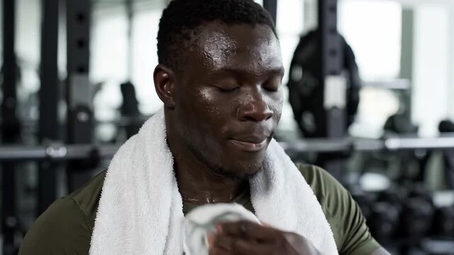 Sweaty man wiping his face with a towel during a gym workout, showing exercise fatigue, recovery, and post workout rest