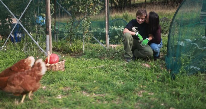 Happy mother and son having tender moment inside vegetable garden - Family people having fun in fall time - Nature, off grid and countryside lifestyle concept - UGC content
