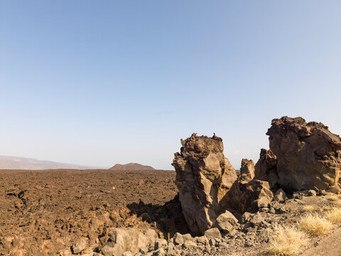 Jagged black lava rock formations rise from a volcanic field with a distant cinder cone, Tadjourah Region, Tadjoura, Djibouti