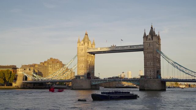 Tour boat passing under Tower Bridge on the River Thames during early evening golden hour in London.