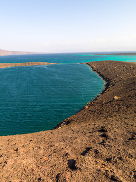 A black volcanic peninsula separates deep blue water from a turquoise lagoon, Tadjourah Region, Goubet Al-kharab, Djibouti