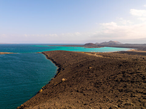 A turquoise lagoon curves along a black volcanic coastline dotted with small huts, Tadjourah Region, Goubet Al-kharab, Djibouti