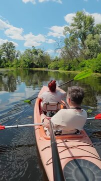 Mature couple paddling orange tandem kayak on calm river promoting teamwork and active lifestyle