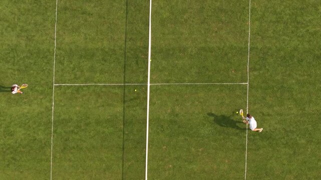 Top down aerial view of two athletes playing tennis on a green grass court