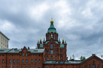 Uspenski Cathedral's red brick façade, green domes and golden cupolas rise over Helsinki's historic center beneath a dramatic cloudy sky, showcasing Russian-influenced Orthodox architecture © photoopus