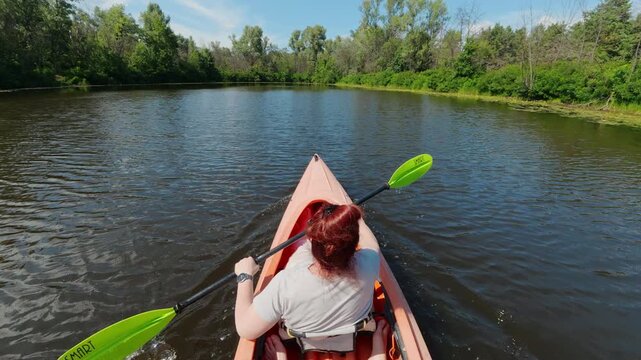 Rear view of woman paddling tandem kayak on rural river for outdoor recreation concept