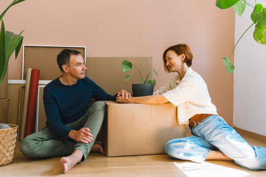 A mature caucasian couple spends time together on the floor surrounded by cardboard moving boxes. Happy family relocation and new property ownership concept.