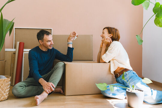 A mature caucasian man cheerfully shows house keys to his smiling wife among unpacked moving boxes. Joyful home buying and successful mortgage approval concept.